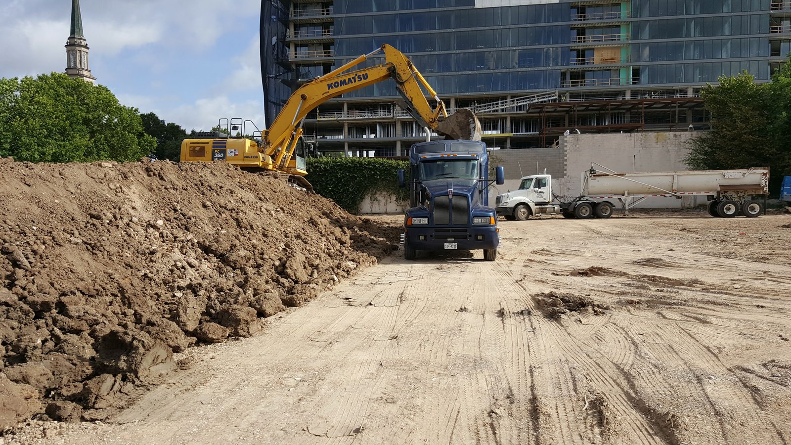 Komatsu excavator loading GMS dump truck at active downtown Houston construction site with city skyline